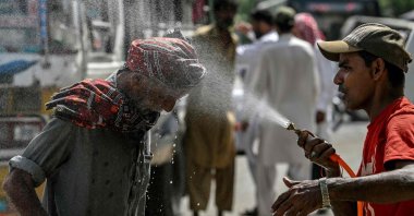 A volunteer sprays water on a passerby's head to cool off on a hot summer day along a road amid the ongoing heat wave, Karachi, Pakistan, April 21, 2025. (AFP Photo)