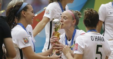 United States' Becky Sauerbrunn (C)  kisses the trophy as Lauren Holiday (L) and Kelley O'Hara look on after the U.S. beat Japan 5-2 in the FIFA Women's World Cup championship, Vancouver, Canada, July 5, 2015. (AP Photo)